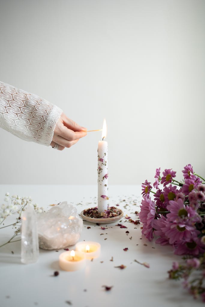 Woman Holding Her Hand near a Burning Candlestick Standing on a Table with Flowers and Crystals